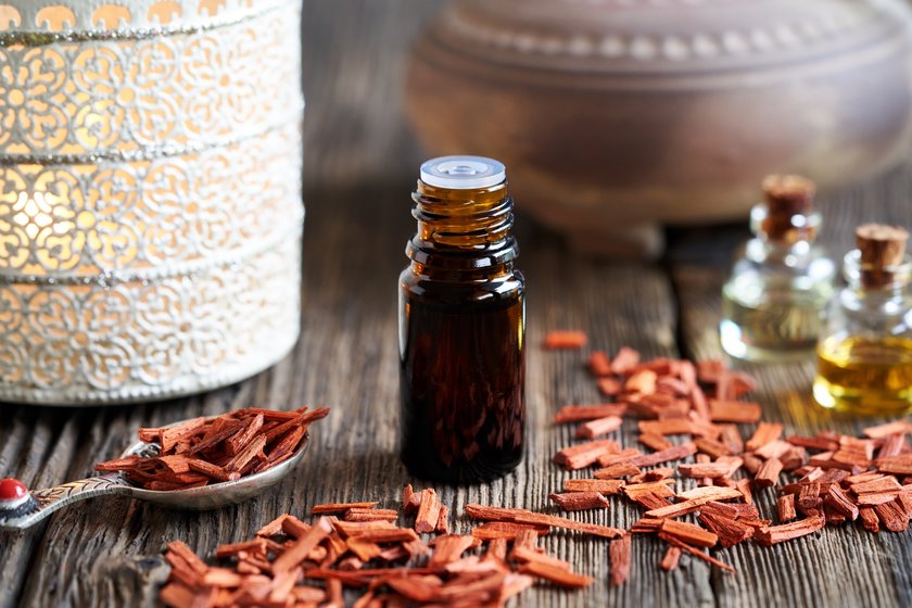 A dropper bottle of aromatherapy essential oil with red sandalwood chips and an aroma lamp in the background