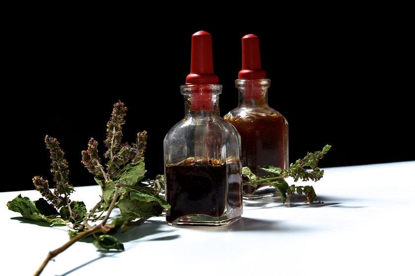 Two small eye dropper bottles with herbal extract essential oils and branch of dried patchouli leaves and flowerss. Oils are patchouli and rosemary.